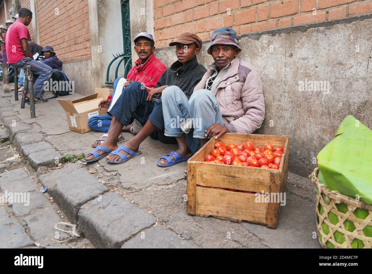 Antananarivo, Madagaskar - 24. April 2019: Drei unbekannte madagassische Männer sitzen auf dem Bürgersteig und verkaufen Tomaten. Essen wird in der Regel auf den Straßen in Madaga verkauft Stockfoto