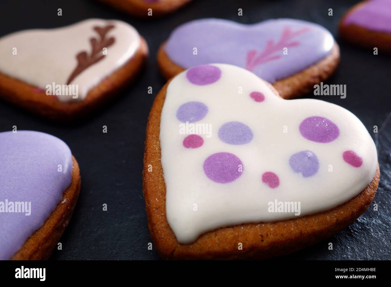 Hausgemachte Kekse in Glasur. Handgemachte Lebkuchenkekse in Herzform auf einem schwarzen Tisch. Nahaufnahme. Geringe Schärfentiefe Stockfoto