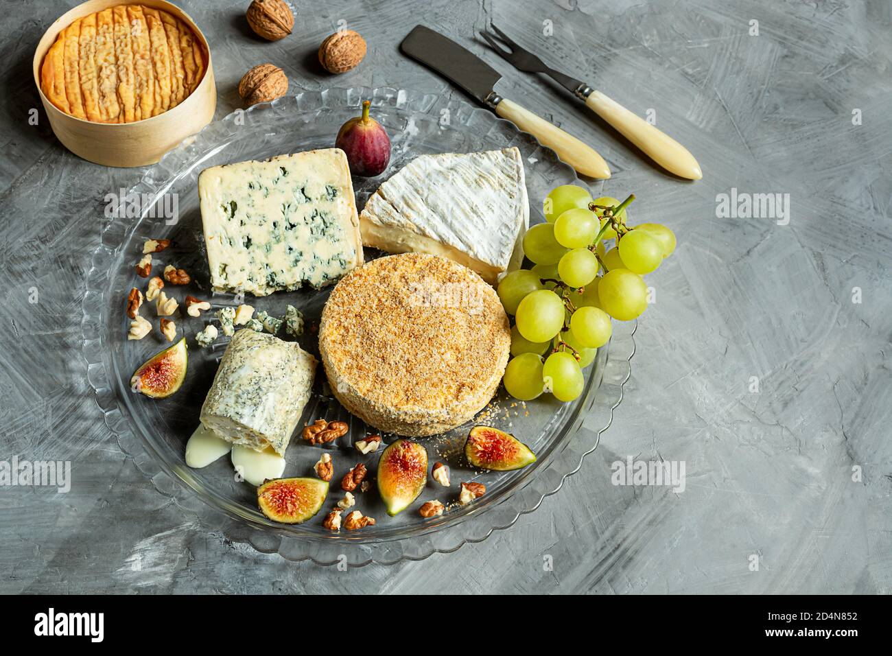 Auswahl an französischem Käse - Camembert, roquefort, Brie, Ziegenkäse und Epoisse mit Trauben, Feigen und Nüssen auf grauem Hintergrund. Draufsicht, Kopierer-SPAC Stockfoto
