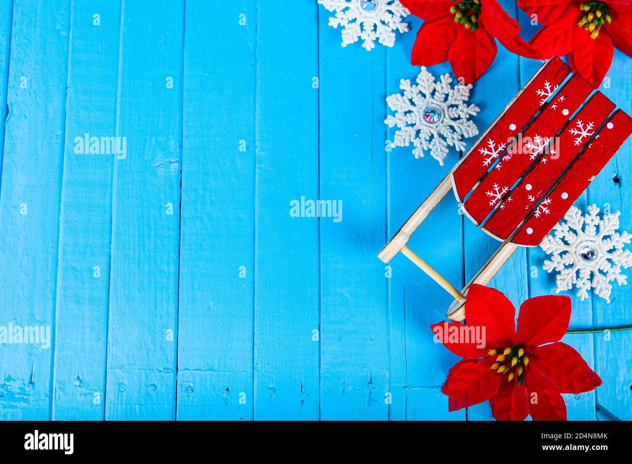 Stillleben zu Weihnachten. Schlitten, Schneeflocken und Weihnachtssterne auf blauem Holzhintergrund, Draufsicht. Stockfoto