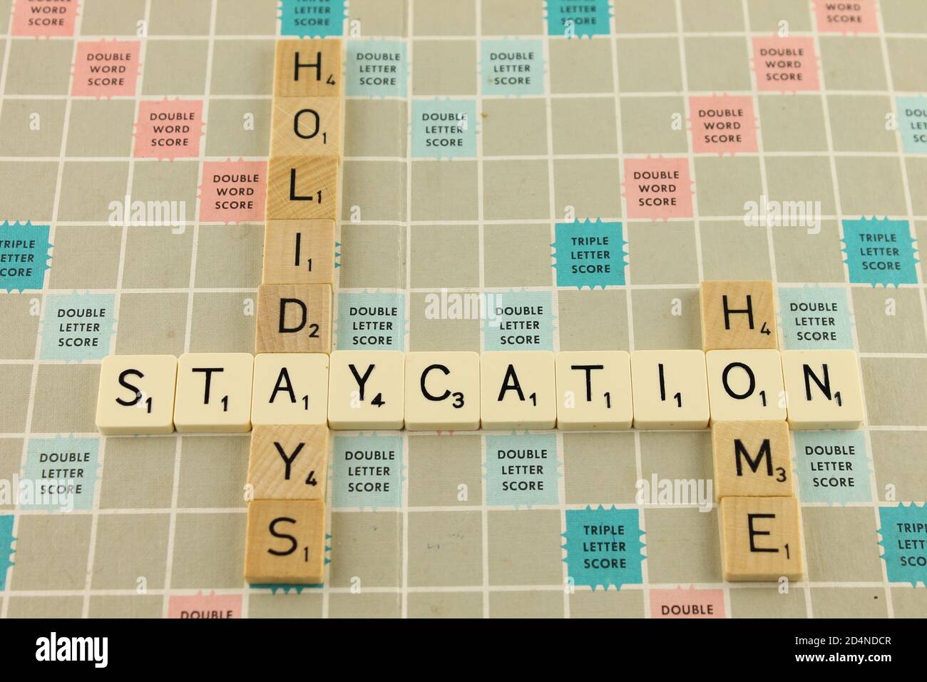 Staycation, Phrase auf einem Schrottbrett in weiß mit den Worten Urlaub und Heimat in braunen Holzfliesen Stockfoto
