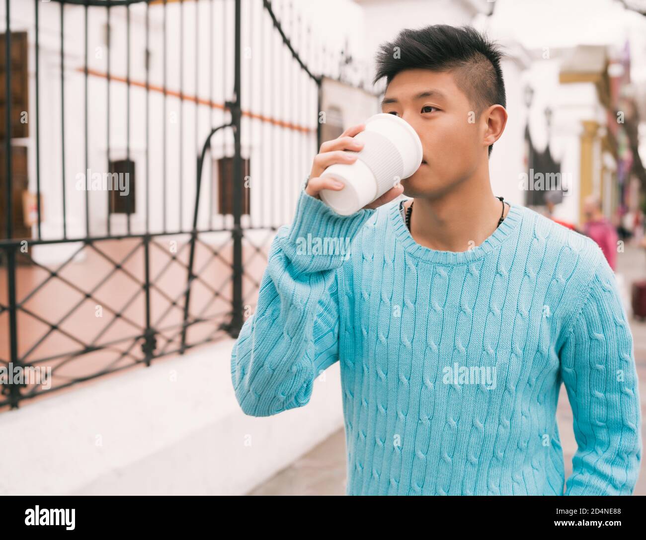Porträt eines jungen asiatischen Mannes, der eine Tasse Kaffee trinkt, während er draußen auf der Straße läuft. Städtisches Konzept. Stockfoto