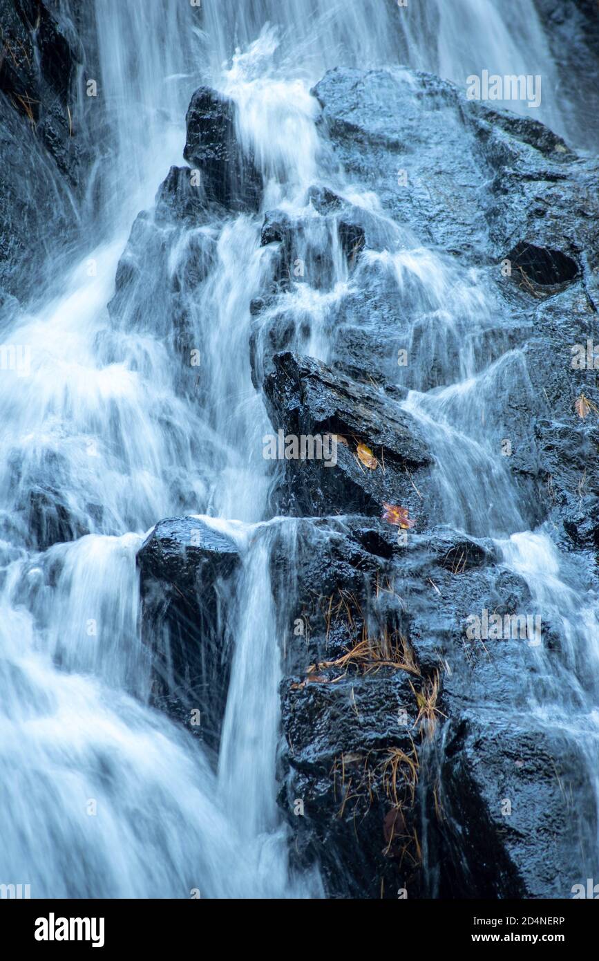 Wasserfall mit langer Belichtung stürzt auf zerklüftete schwarze Felsen ab. Stockfoto