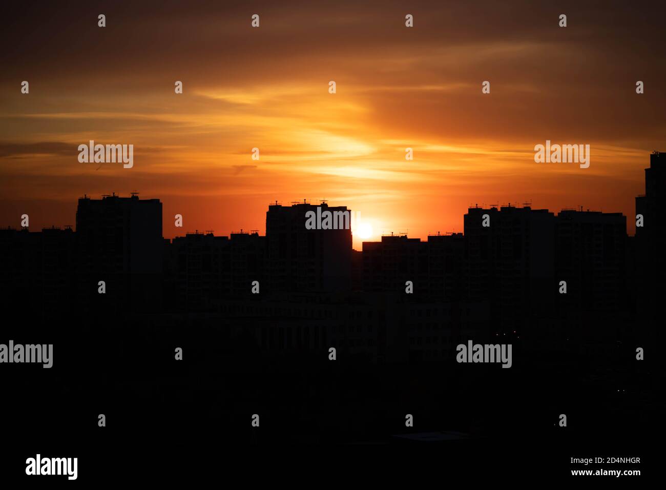 Große Stadt in den Strahlen des Sonnenuntergangs. Hohe schwarze Häuser und rot-feuriger Himmel. Stockfoto