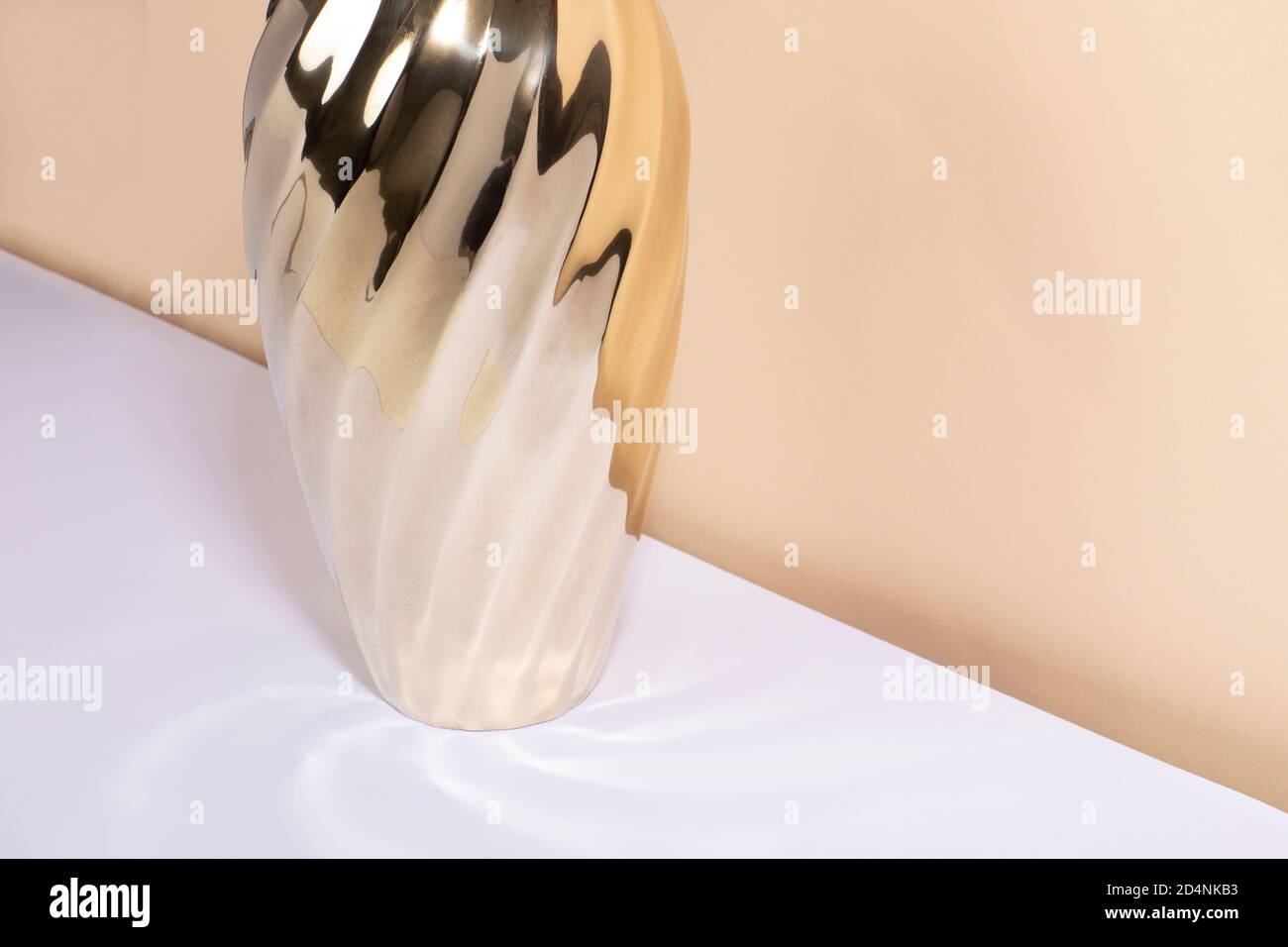 Ein Vintage Messing Objekt mit viel Glanz und geschwungenen Kanten stehen auf einem weißen Tisch und einem beigen Hintergrund. Moderner Stil aus der Mitte des Jahrhunderts, goldenes Interieur Stockfoto
