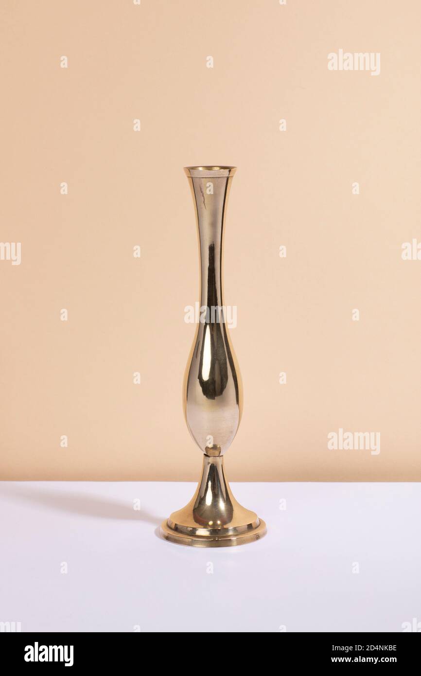 Eine Vintage Messingvase mit viel Glanz und einer geschwungenen Form, die auf einem weißen Tisch und einem beigen Hintergrund steht. Moderner Stil aus der Mitte des Jahrhunderts, goldenes Interieur Stockfoto