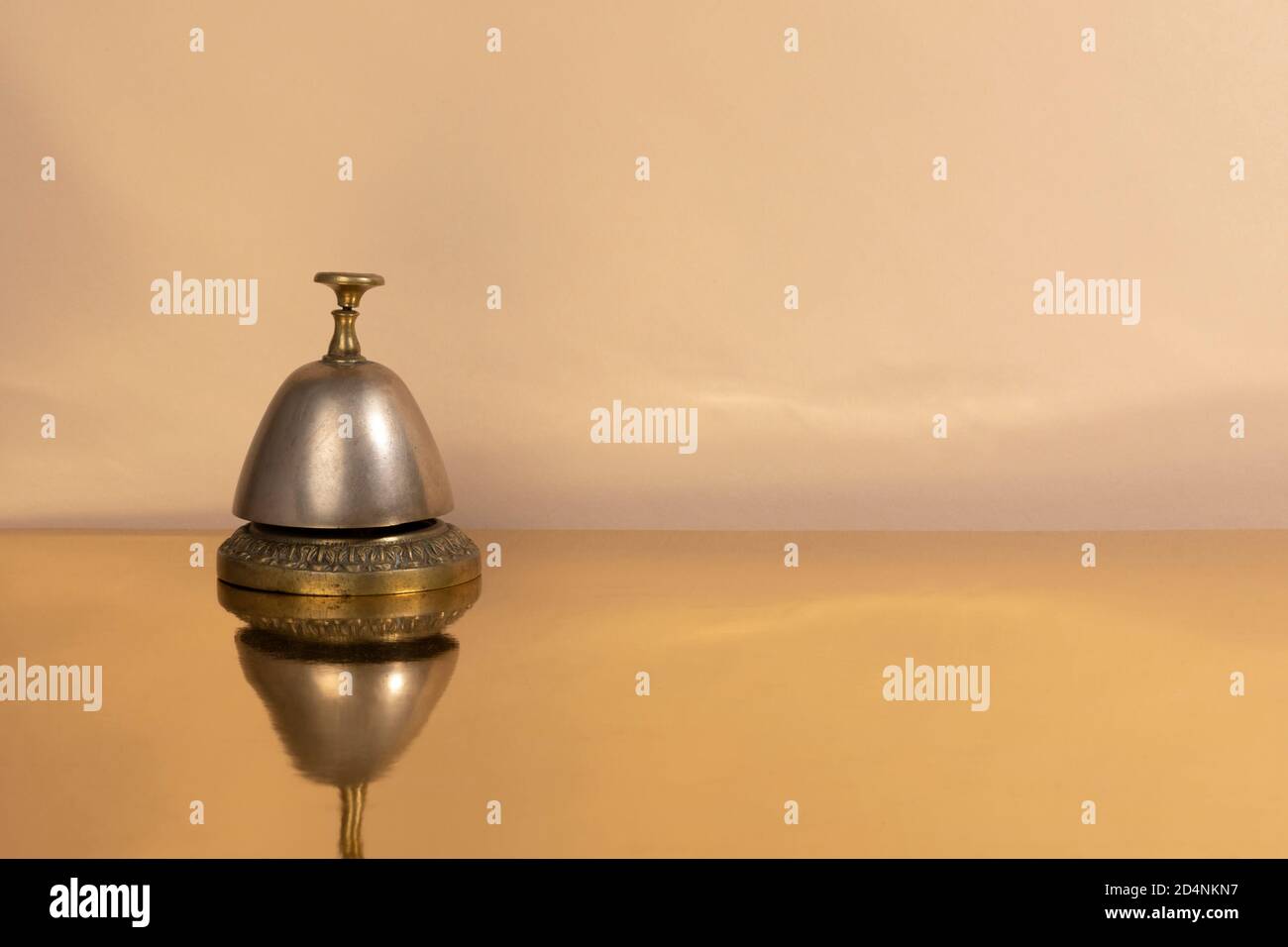 Eine alte Vintage-Messingkellner oder Empfangsdame Glocke isoliert auf einem goldenen reflektierenden Tisch und einem beigen Hintergrund. Studio mit warmen Farben aufgenommen Stockfoto