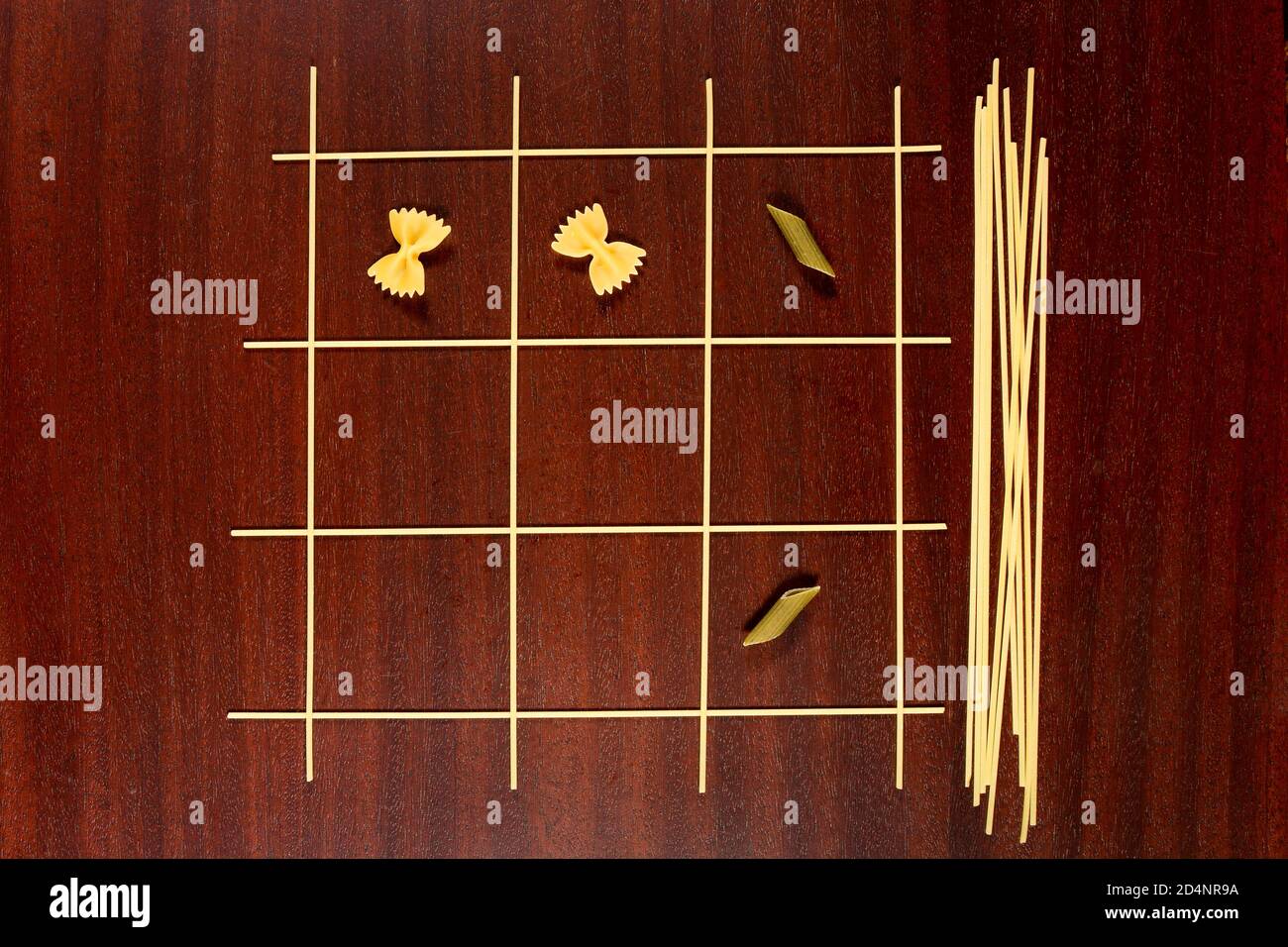 Italienische Pasta. TIC Tac Toe oder XS und OS Spiel aus rohen Spaghetti, Farfalle und Penne gemacht. Trocknen Sie Makkaroni und Capellini auf einem braunen Holztisch. Stockfoto