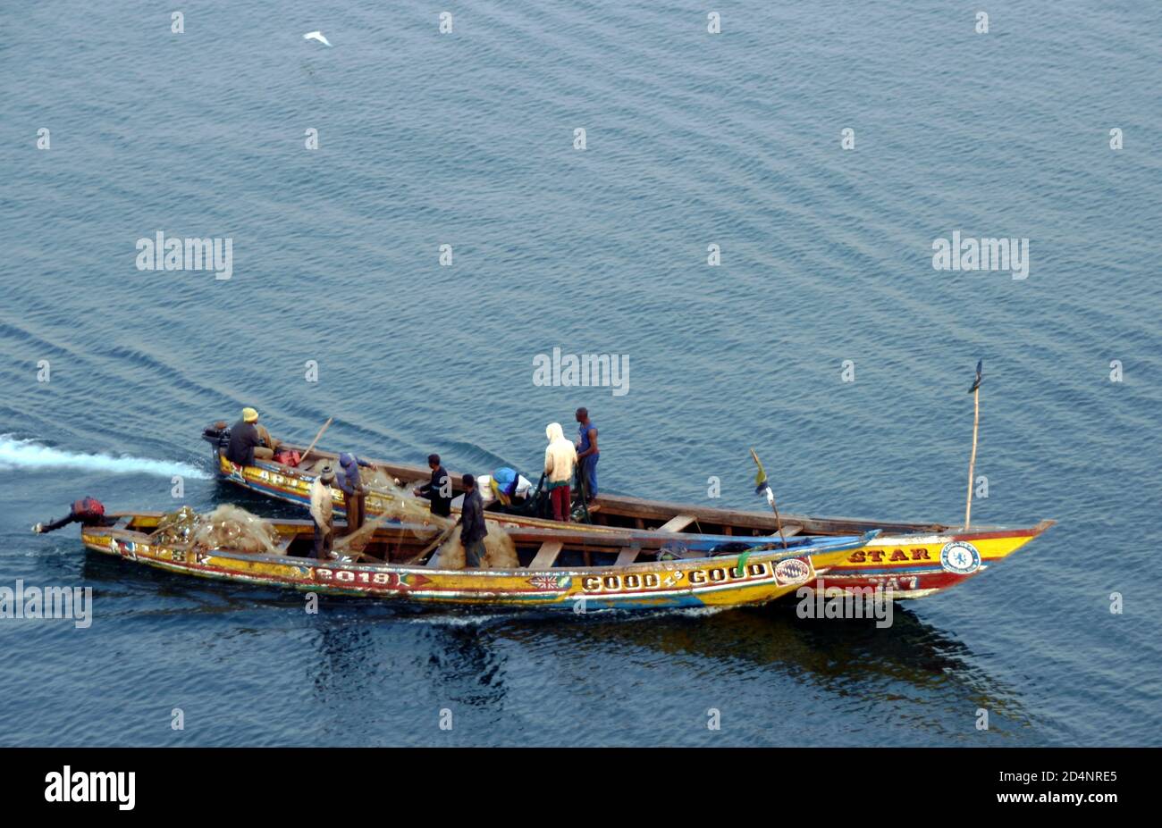 Alte hölzerne, viele farbige Fischerboote, die mit einheimischen afrikanischen Einheimischen bemannt sind, die in der Nähe von Freetown in Sierra Leone zum Fischfang gehen und Netze vorbereiten. Stockfoto