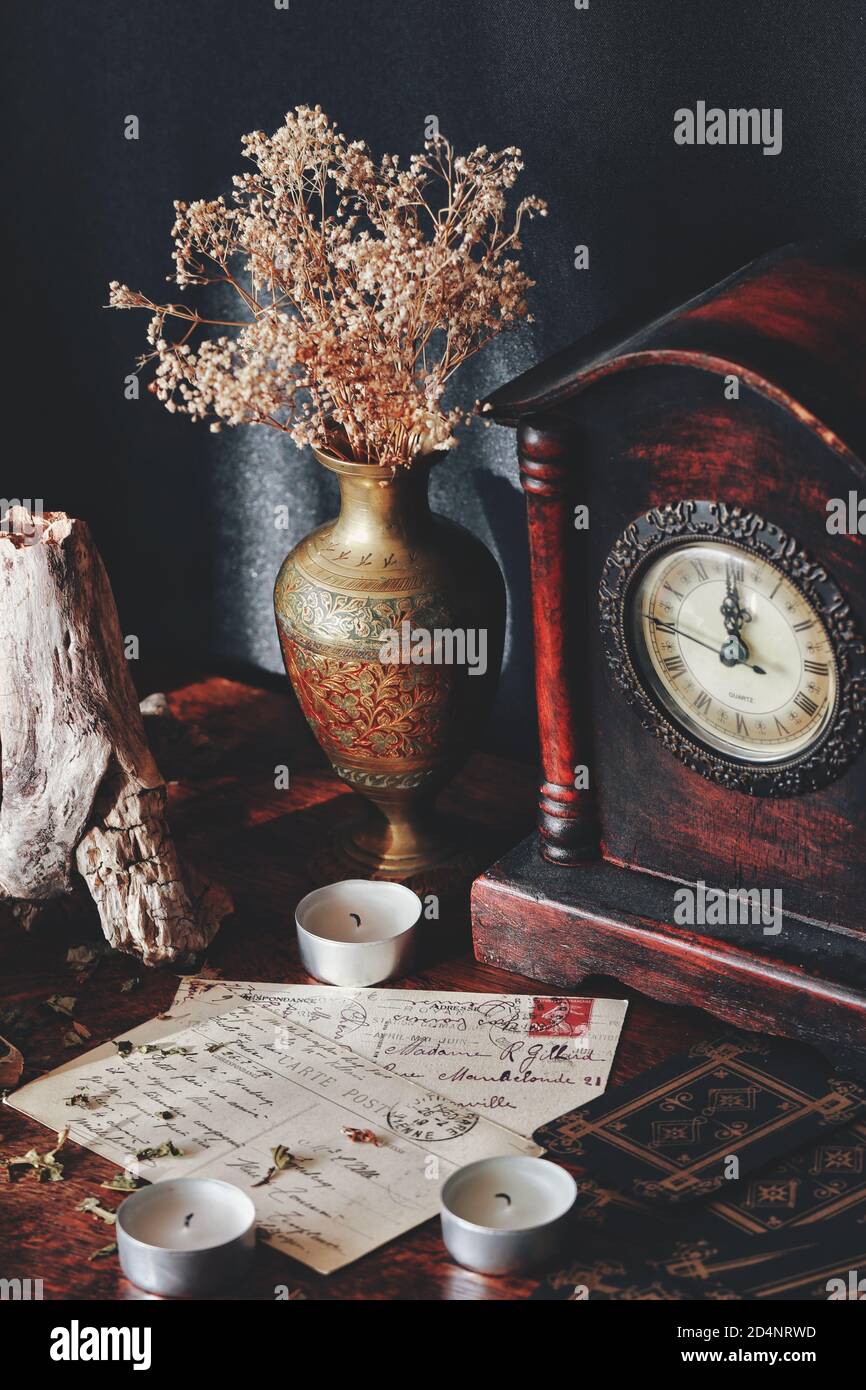 Vintage Postkarten mit kursiver Handschrift auf dunklem Holztisch. Rustikale Stimmung mit Kerzen, alte antike Uhr, Messing getragene Vase Stockfoto