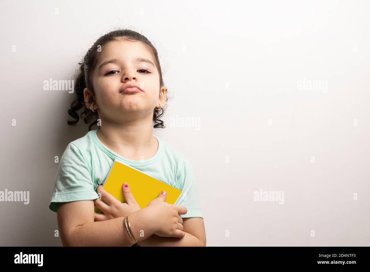 Kleines Mädchen hält ein Kinderbuch mit leerem Einband vor dem Körper, editierbare Modell-up-Serie Vorlage bereit für Ihr Design, Auswahlpfad enthalten Stockfoto