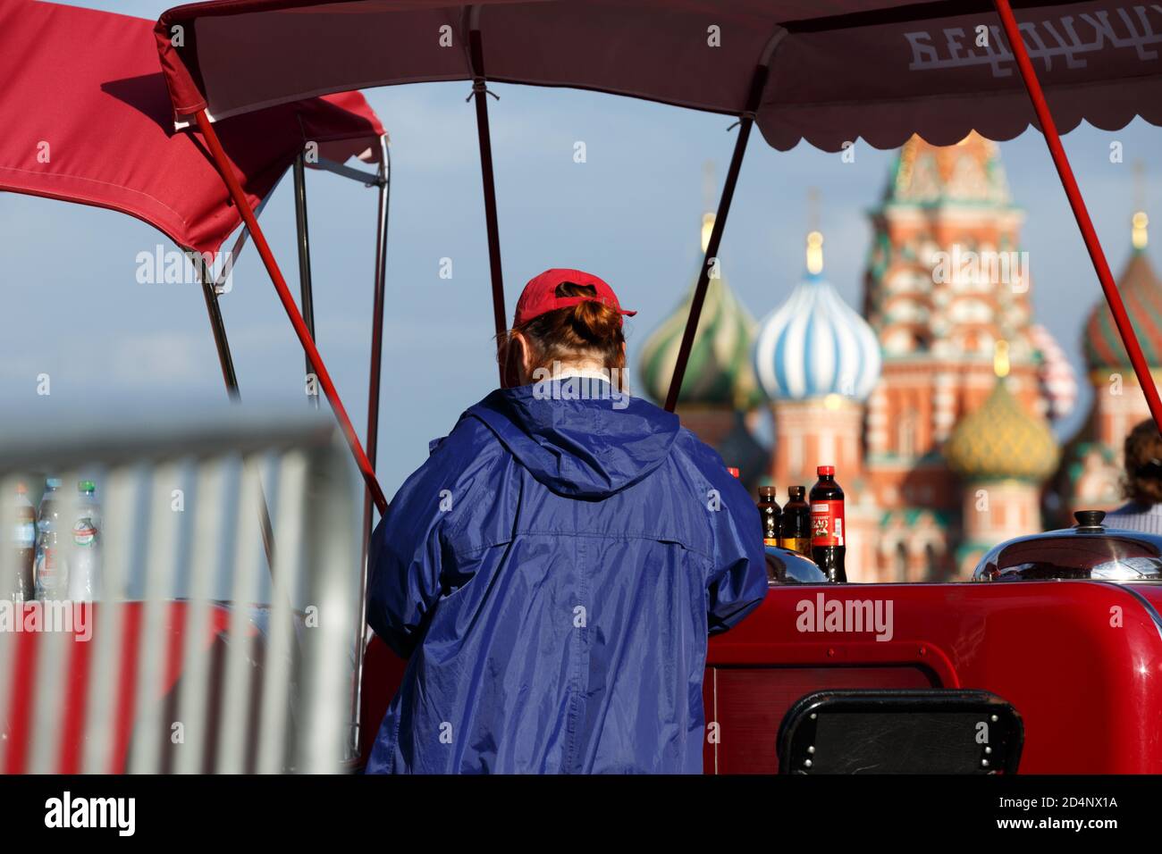 Moskau, Russland, Juli 21,2020: Eisverkäufer in blauer Kleidung im mobilen roten Kiosk, der Eiscreme auf dem roten Platz mit Blick auf die Basilius-Kathedrale verkauft Stockfoto
