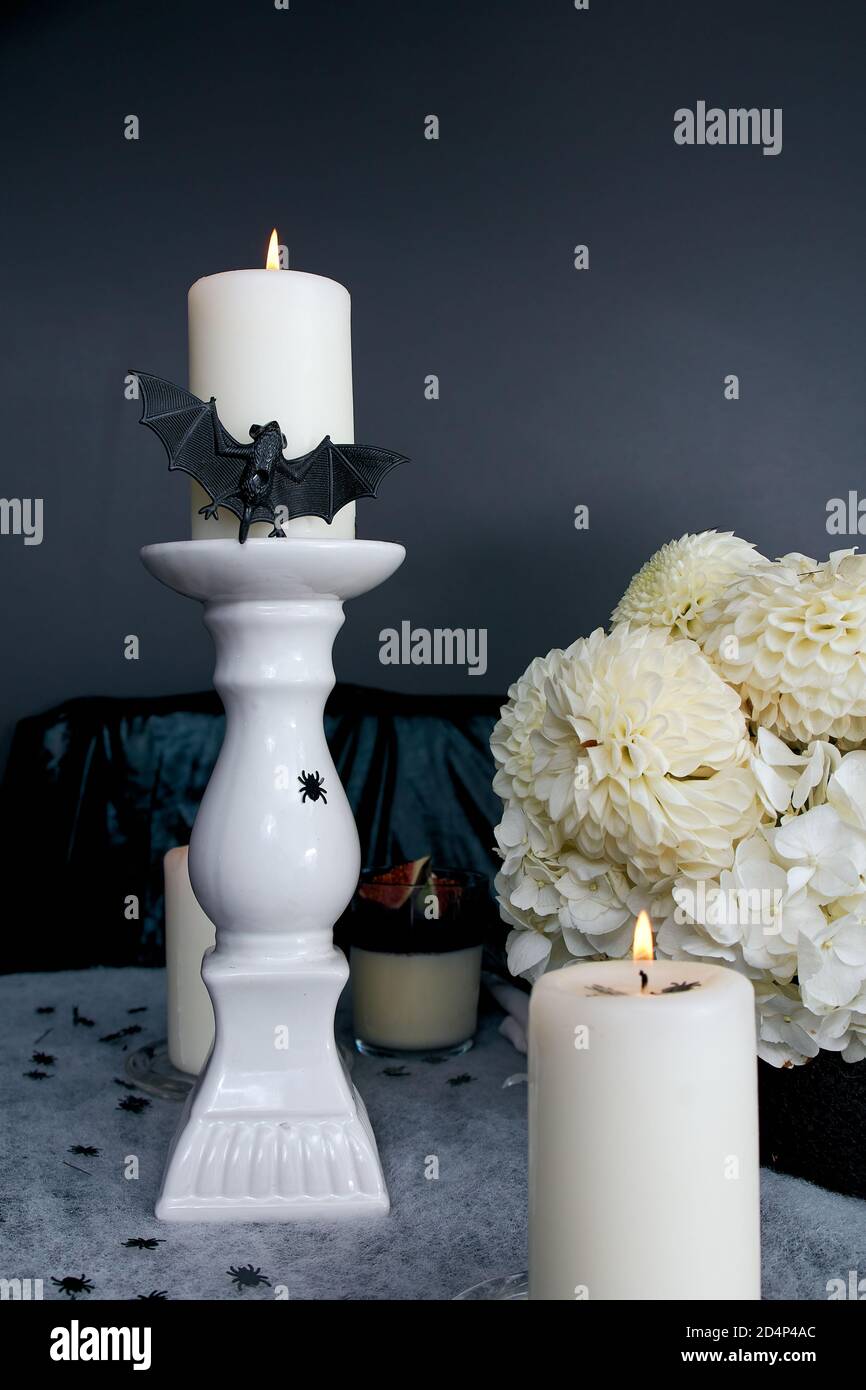 Halloween-Dekorationen. Brennende Kerzen. Die Partitur auf einem hohen ist suspendiert und mit einer Fledermaus verziert. Bouquet und ihre Chrysanthemen und gortesias. Stockfoto