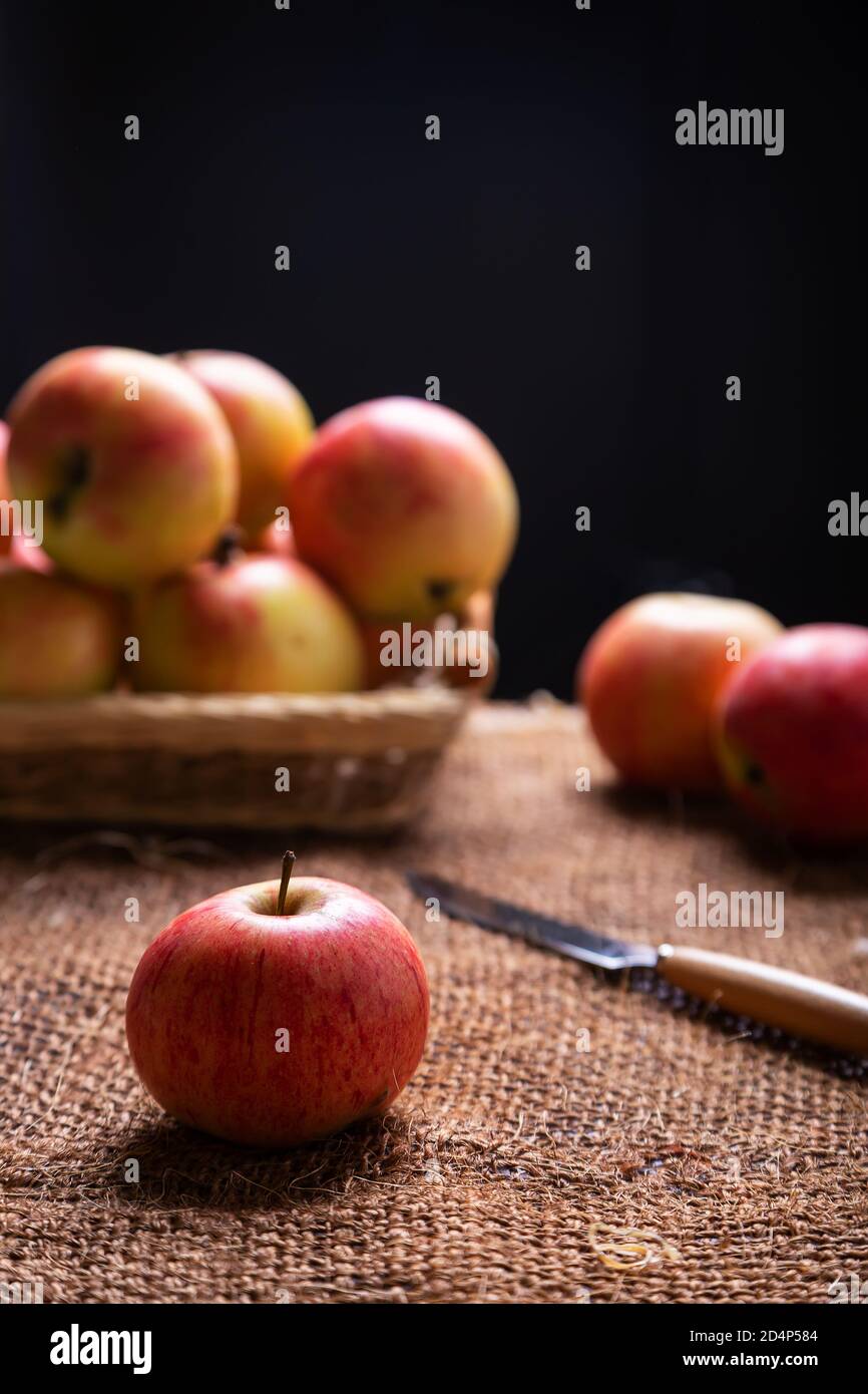 Reife Äpfel auf Sackleinen und in einem Korb auf schwarzem Hintergrund. Hintergrundbeleuchtung. Rustikaler Stil, Nahaufnahme. Stockfoto