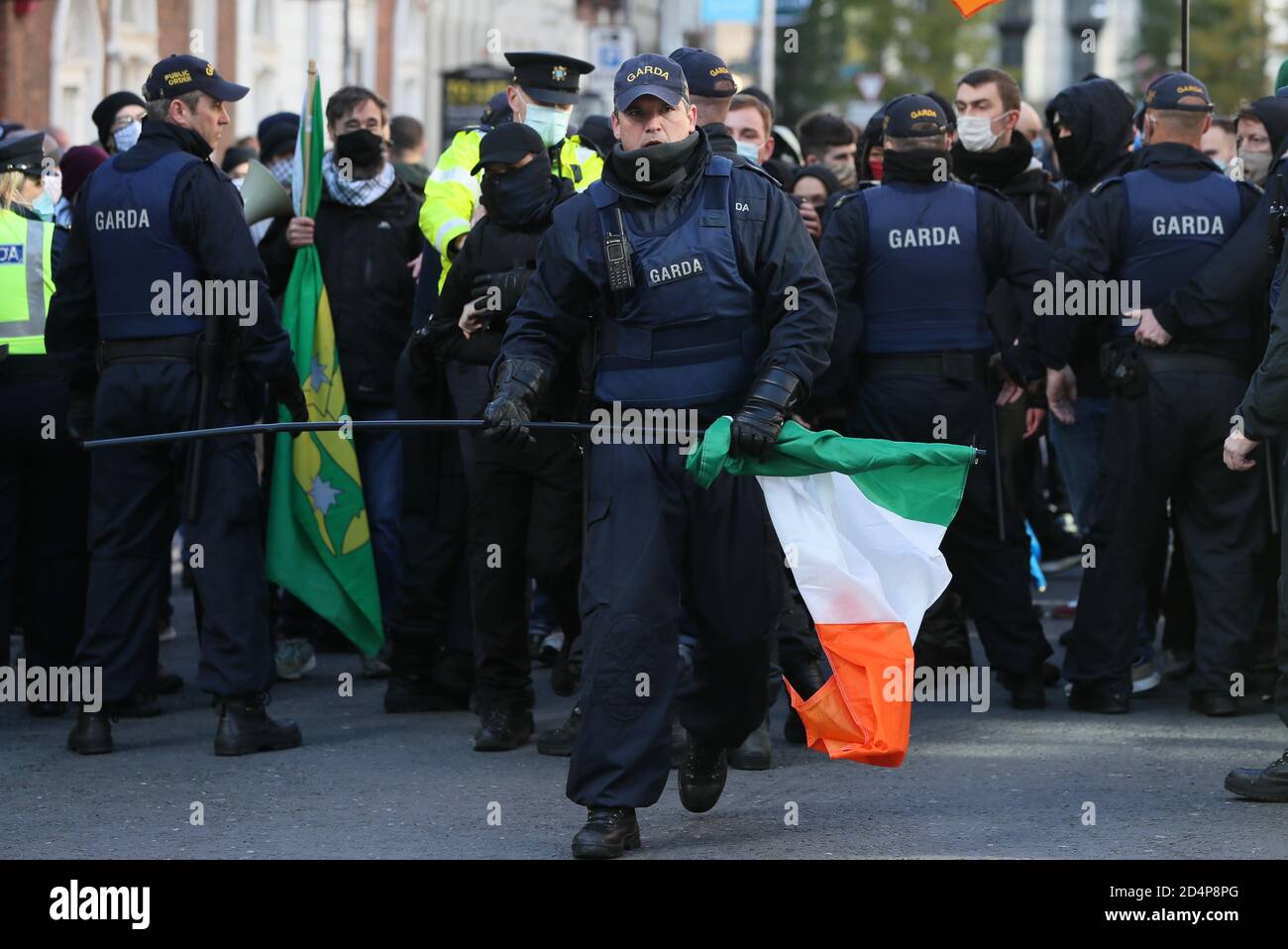 Ein Mitglied der Garda Public Order Unit entfernt während eines Anti-Lockdown-Protests vor dem Leinster House in Dublin eine irische Trikolore von den Gegendemonstrierenden, da Irland weiterhin landesweit an einer Stufe-3-Coronavirus-Sperre versperrt ist. Stockfoto