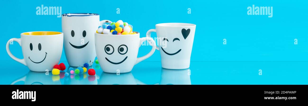 Vier Tassen mit lustigen Gesichtern auf einem farbigen Hintergrund. Das Konzept eines freundlichen Unternehmens, einer großen Familie, Treffen mit Freunden für eine Tasse Tee oder Kaffee. Lächeln Stockfoto
