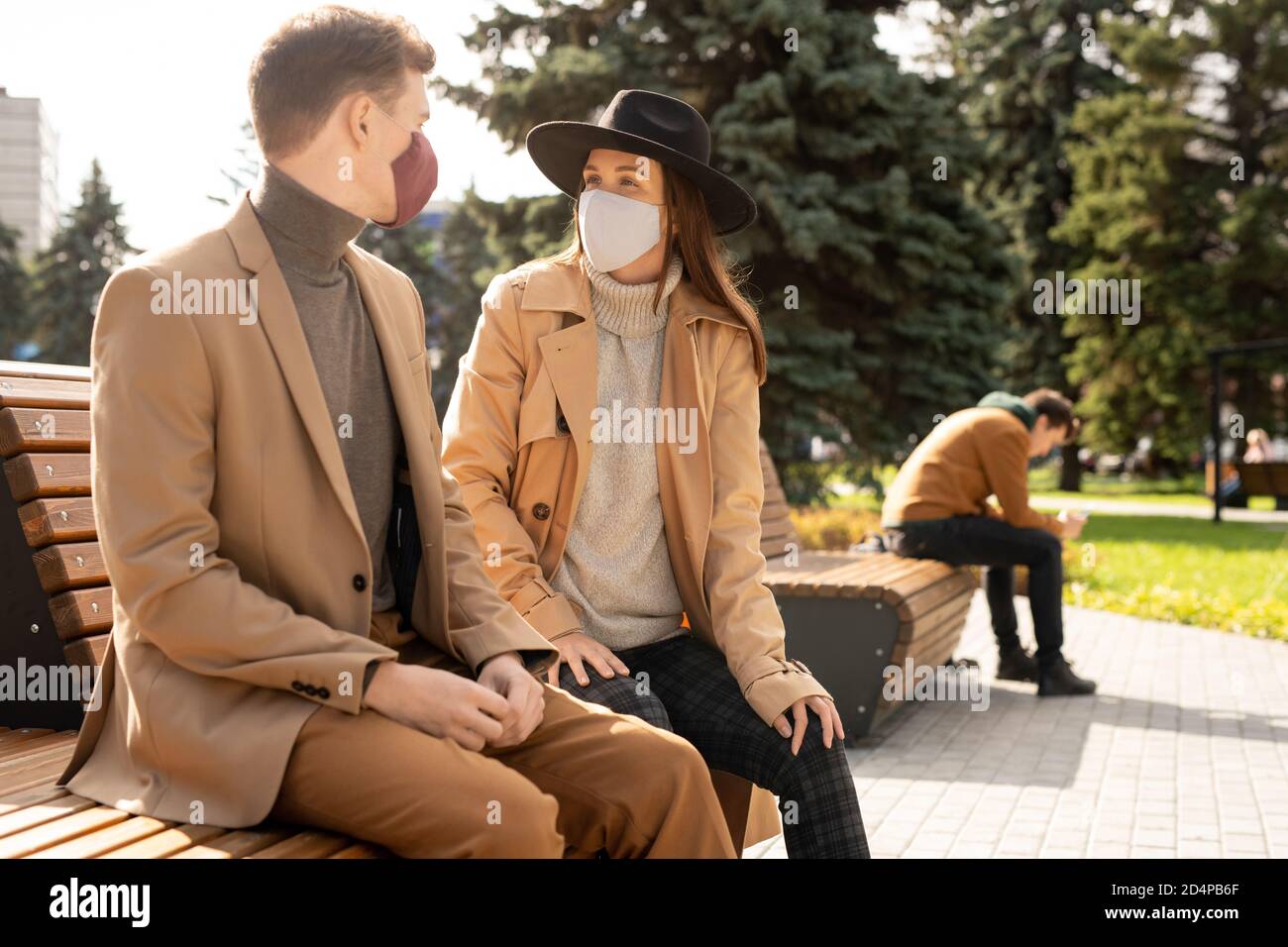 Glücklich junge stilvolle Paar in Schutzmasken entspannen auf der Bank Im Park Stockfoto