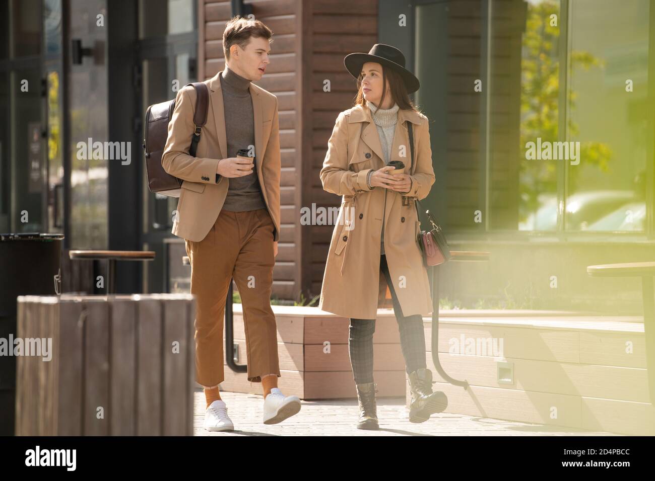 Junge ernsthafte stilvolle Frau mit Getränk im Gespräch mit ihrem Freund In Casualwear Stockfoto