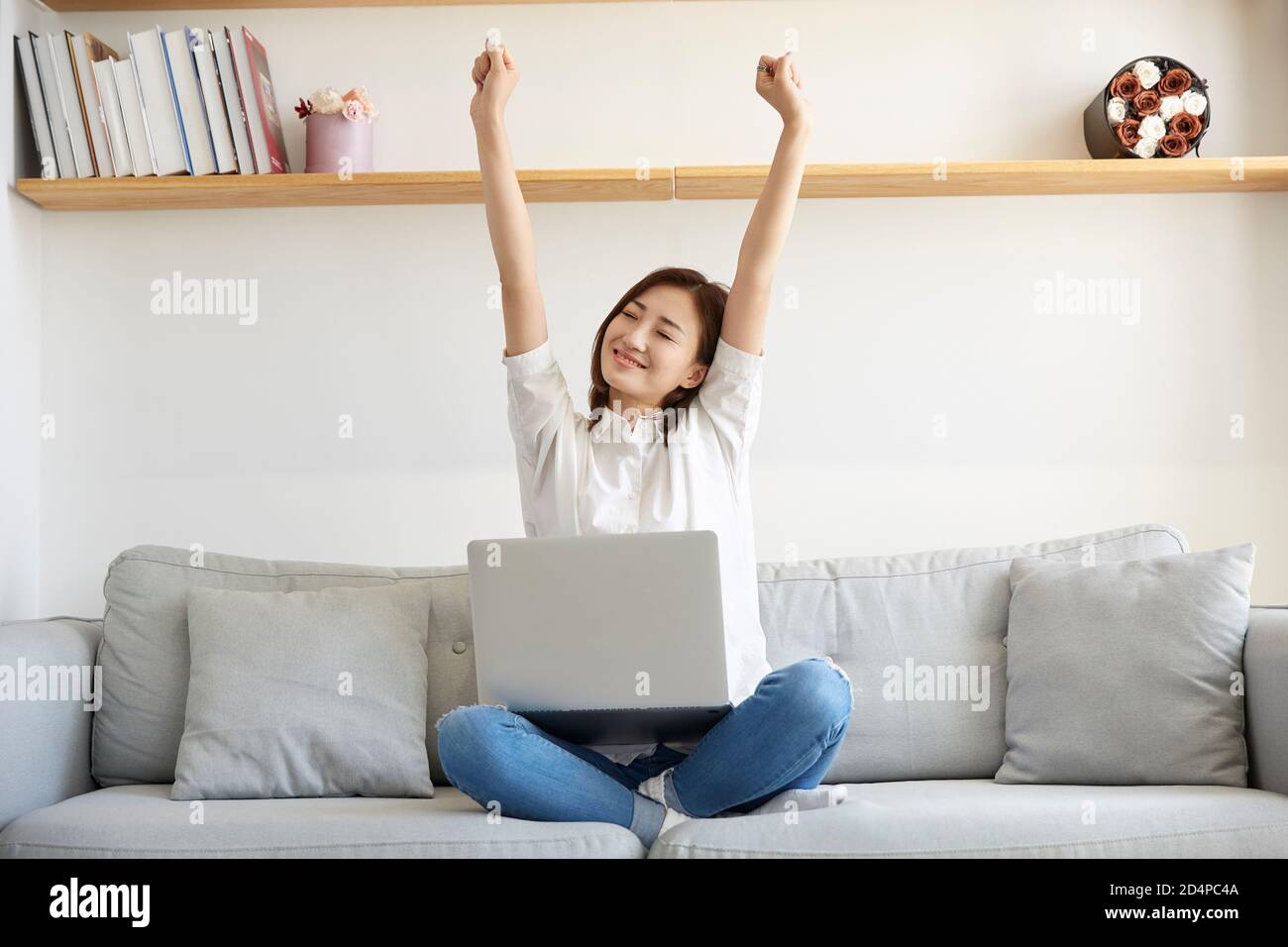 Junge asiatische Geschäftsfrau, die von zu Hause aus auf der Couch sitzt Streckt die Arme glücklich und lächelnd Stockfoto
