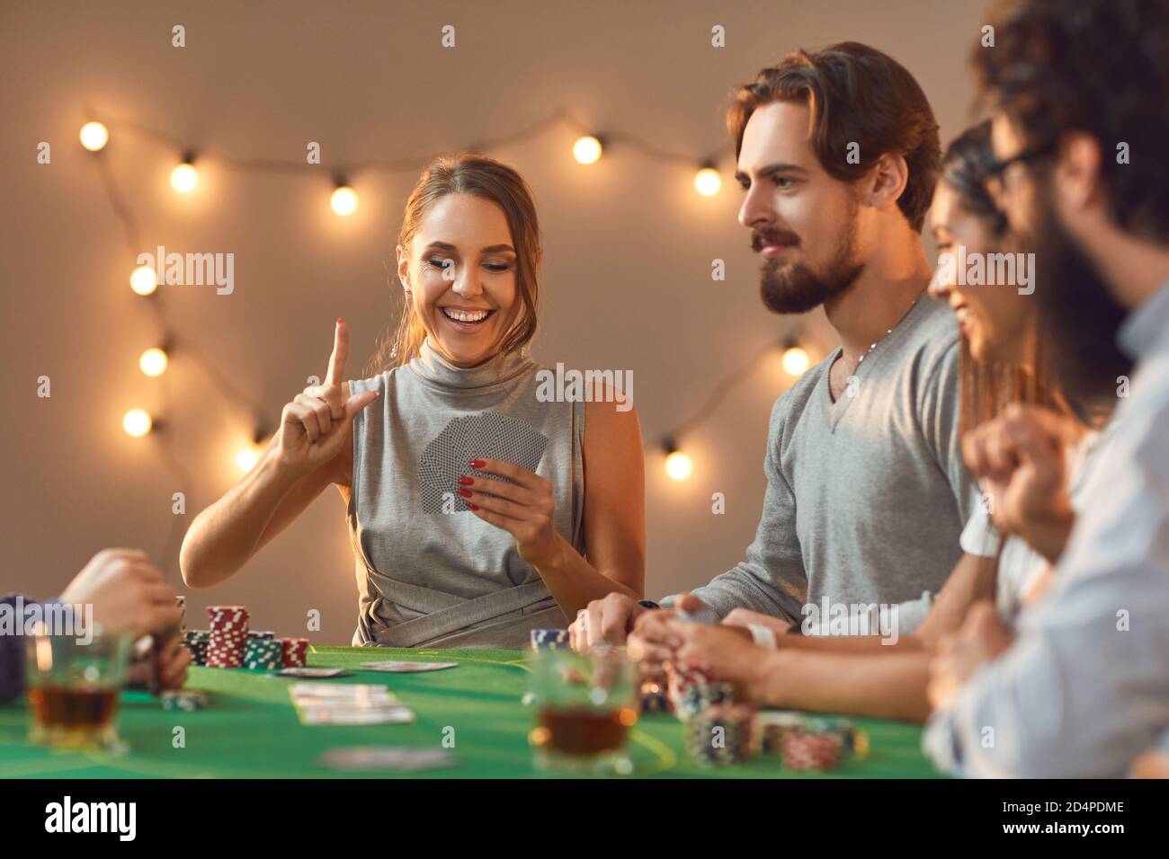 Glückliche junge Frau hält den Finger, wie sie Glück hat Hand in Poker-Spiel mit Freunden Stockfoto
