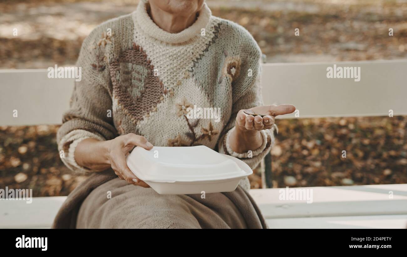 Obdachlose Frau mit Wohltätigkeitsessen und einigen Münzen in der Hand, die im Herbst auf der Bank sitzt. Hochwertige Fotos Stockfoto