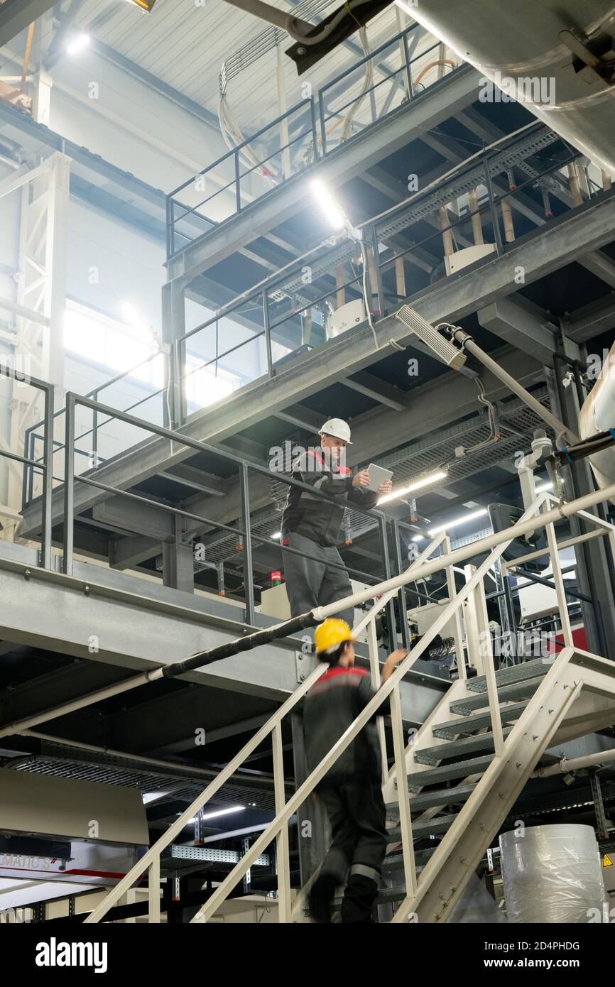 Vorarbeiter mit Tablette biegen über Treppe, wo weibliche Arbeiter bewegen Nach oben Stockfoto