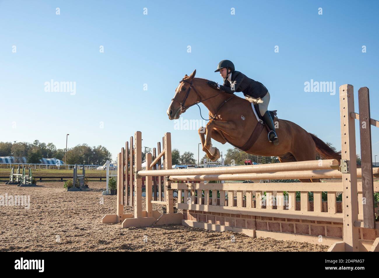 Mädchen im Alter von Teenagern, die auf dem Pferd reiten und beim Springwettbewerb ein Hindernis überwinden. Stockfoto