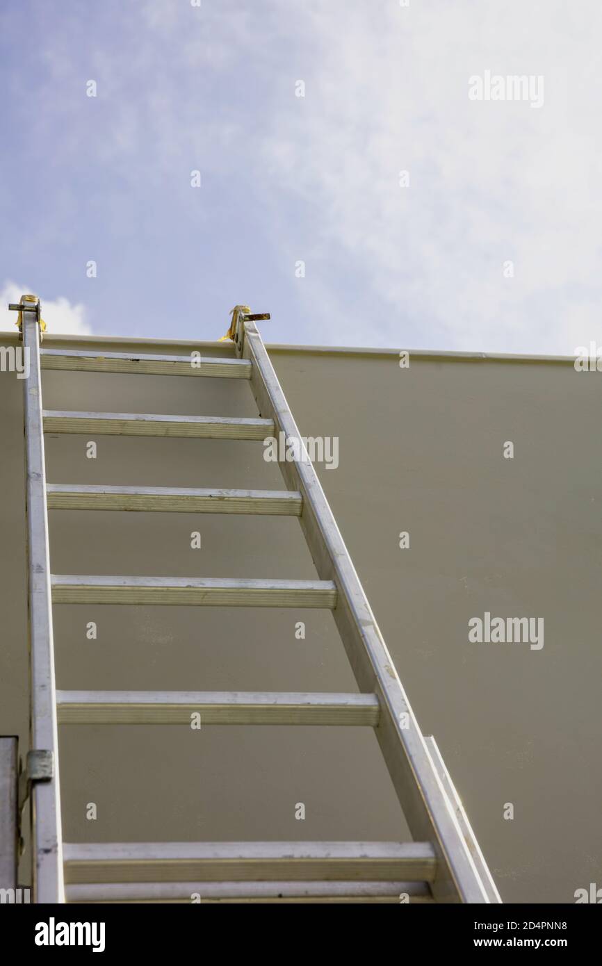 Leiter zum Himmel. Aluminium-Trittleiter gegen graue Wand, blauer Himmel Hintergrund Stockfoto