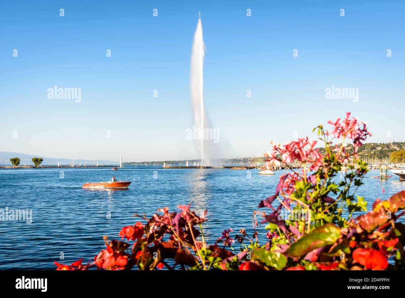 Der Jet d'Eau in der Bucht von Genf, Schweiz, ein Brunnen mit einem 140 Meter hohen Wasserstrahl, Wahrzeichen der Stadt, mit einem Mahagoni-Schnellboot und Blumen Stockfoto