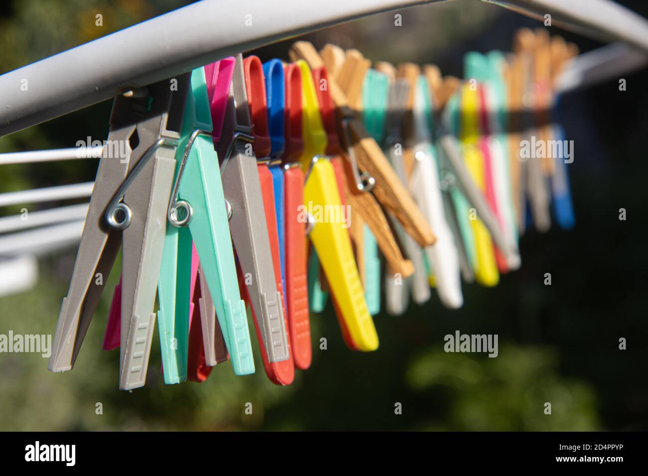 Eine farbige Kleidung hängt an einem Trockengestell Draht. Eine Gruppe von Wäscheklammern in der Schlange am Stand im sonnigen Garten. Stockfoto
