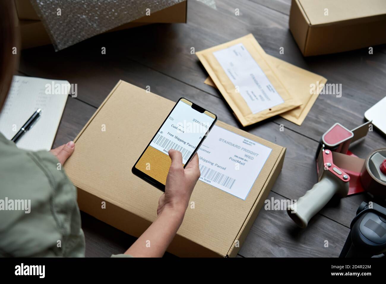 Weibliche Lagerarbeiterin scannt Barcode auf Versandkarton auf dem Smartphone. Stockfoto