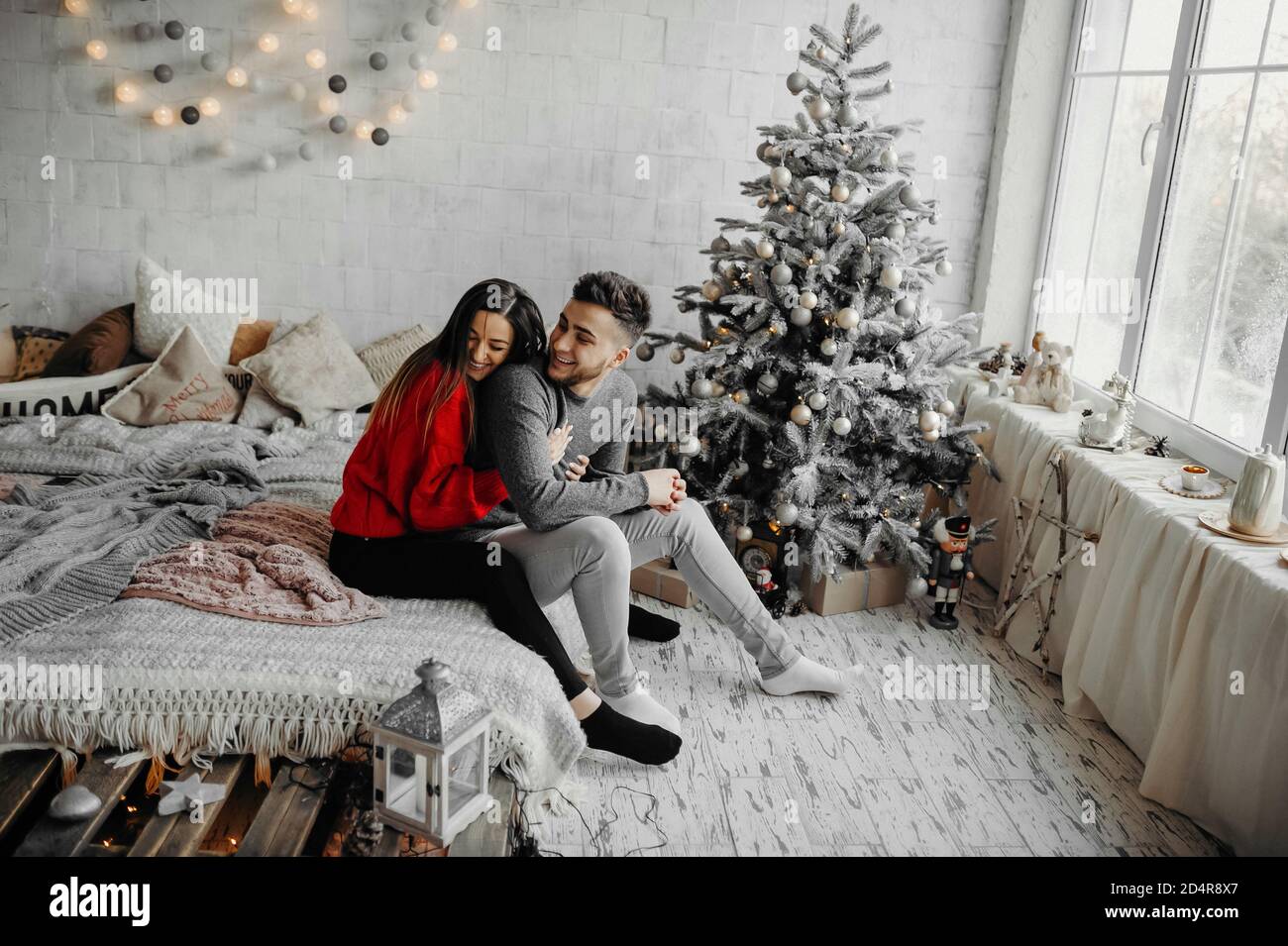 Junge glückliches Paar Spaß auf gemütliches Bett liegen und lachen, Frau umarmt ihren Freund verbringen Winterurlaub zu Hause in warmen weihnachtsatmosphäre Stockfoto
