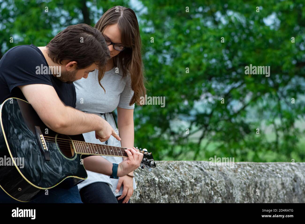 Bruder lehrt Schwester Gitarre in der Natur zu spielen Stockfoto