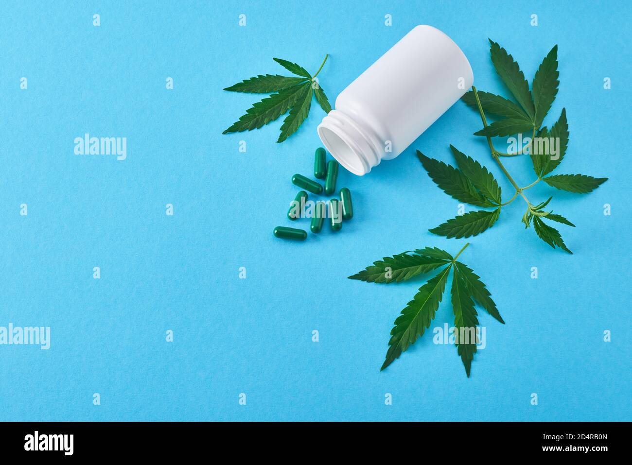 Draufsicht auf eine weiße Flasche mit verschütteten Kapseln darunter Hanfblätter Stockfoto