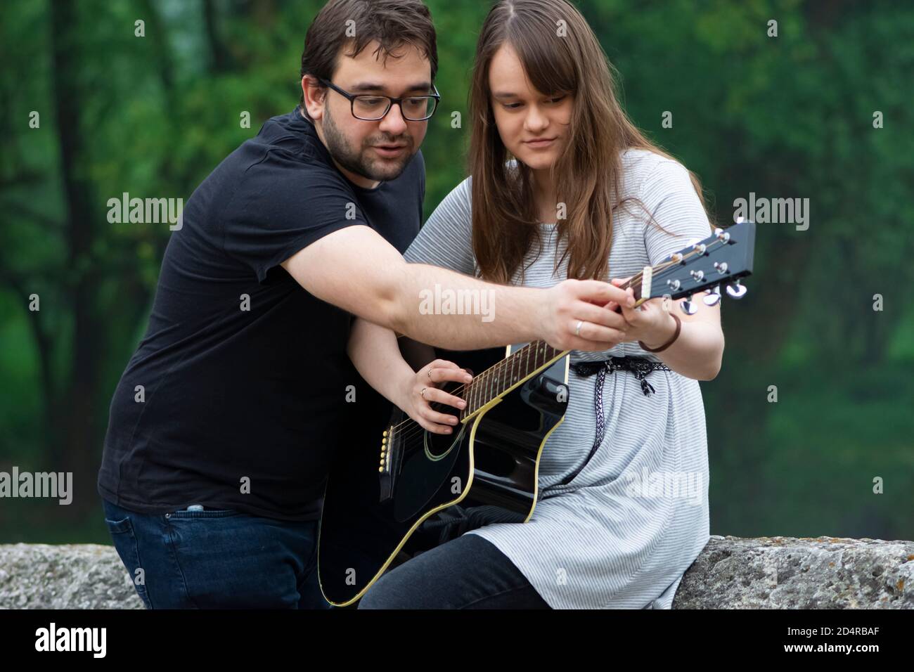 Bruder lehrt Schwester Gitarre in der Natur zu spielen Stockfoto