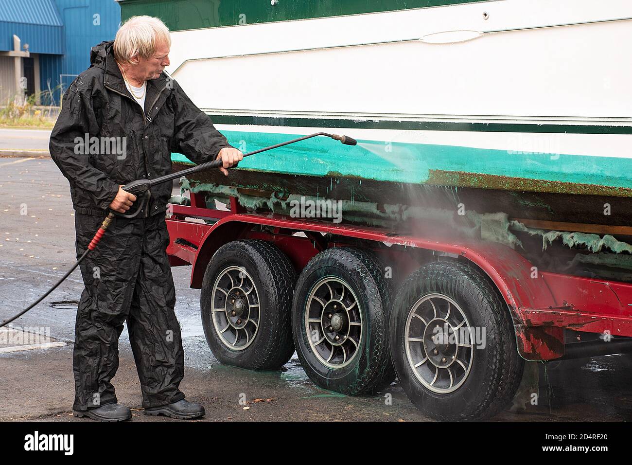Kaukasischer Mann Druck waschen schmutziges Boot auf Anhänger auf Bürgersteig Stockfoto