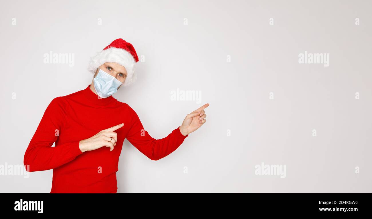 Weihnachten während der Pandemie des COVID-19 Coronavirus-Konzepts. Schöner Mann trägt Einweg-Gesichtsmaske und Santa Hut. Männliche Modell trägt roten Pullover Stockfoto