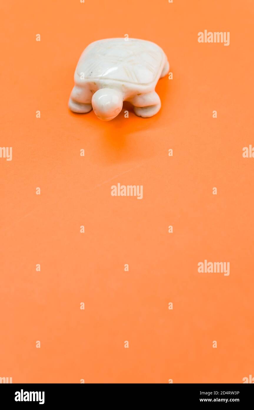 Vertikale Aufnahme einer weißen Schildkrötenstein Figur isoliert auf Ein orangefarbener Hintergrund Stockfoto