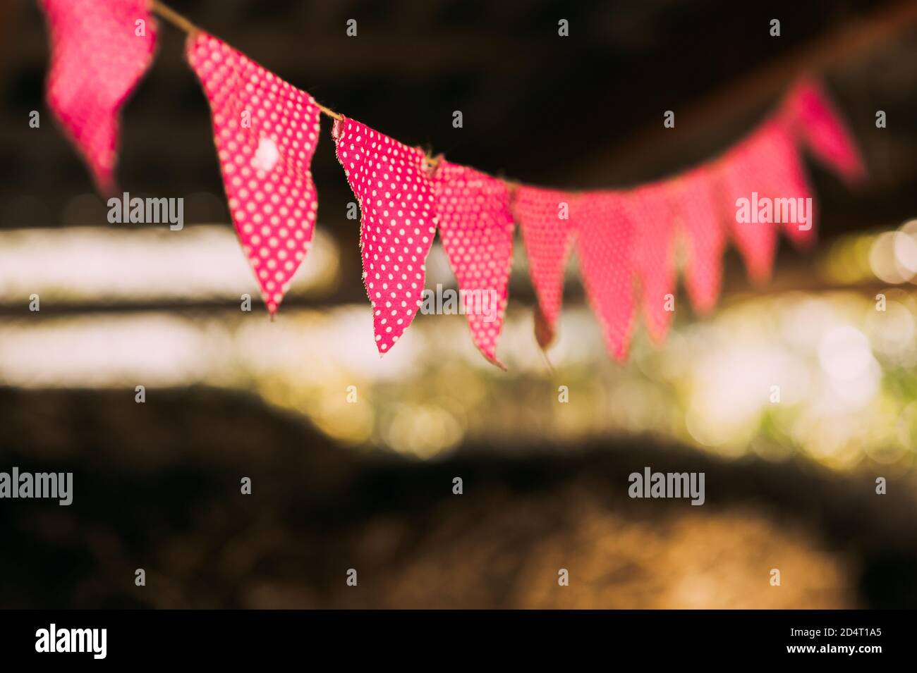 Nahaufnahme von Retro-Girlande mit bunten roten Fahnen mit weißen Punkten bei Sonnenuntergang im Sommergarten. Stockfoto