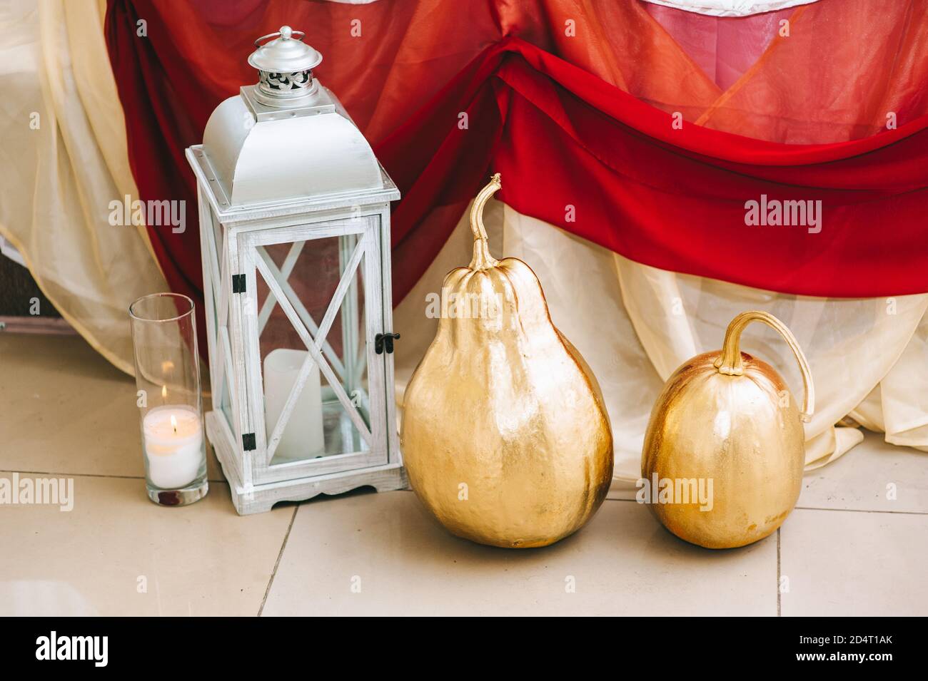 Kürbisse in Gold gemalt stehen auf dem Boden in der Halle neben einem großen hölzernen weißen Kerzenständer. Stockfoto