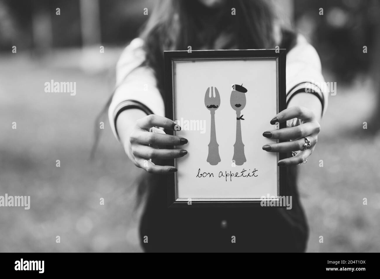 Hände eines gesichtslosen Mädchens halten ein Bild in einem Rahmen mit der Aufschrift bon Appetit. Stockfoto