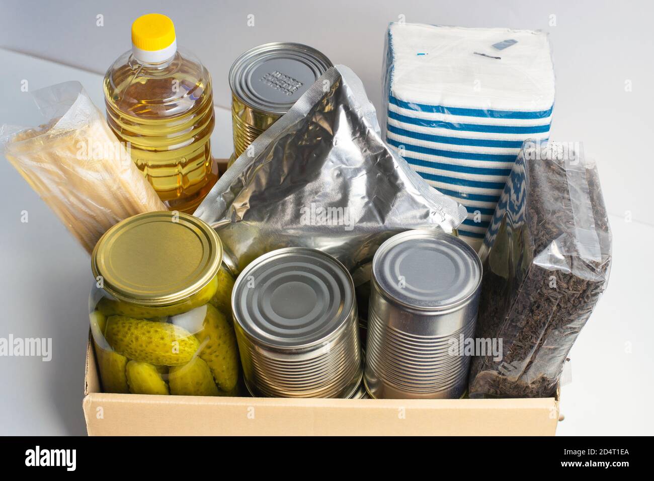 Box mit Essen für eine wohltätige Spende. Konserven, Nudeln, eingelegte Gurken, Pflanzenöl, Tee. Papierservietten. Konzept der Lebensmittelzustellung oder Lebensmittelspende Stockfoto