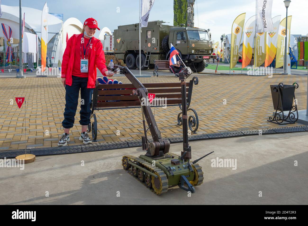 MOSKAU, RUSSLAND - 25. AUGUST 2020: Ein ferngesteuerter militärischer Sapper-Roboter versorgt ein ehrenamtliches Mädchen mit einer Flasche Wasser Stockfoto
