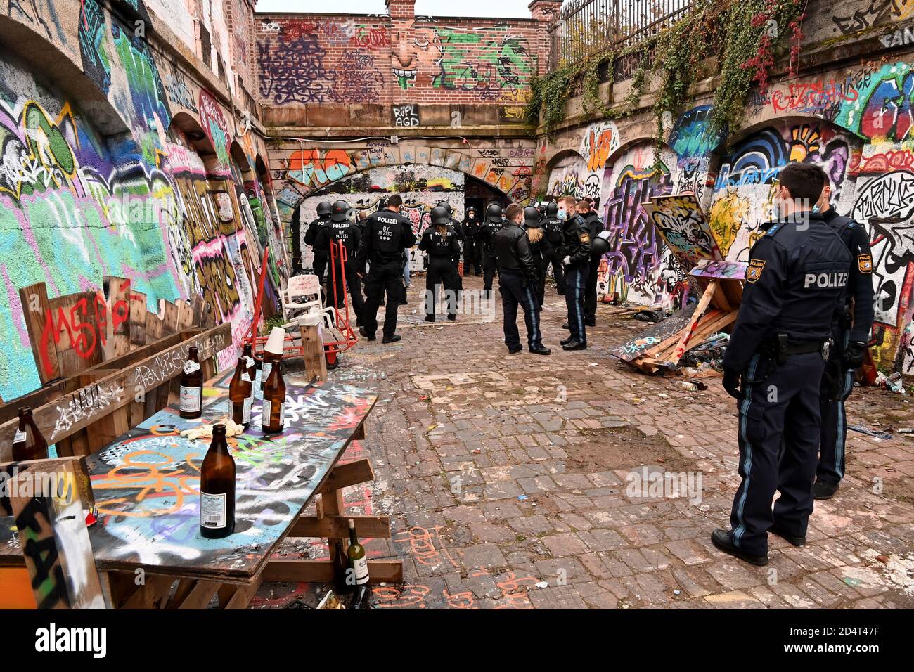 München, Deutschland. Oktober 2020. Polizeibeamte stehen in den frühen Morgenstunden auf einem mit unzähligen Flaschen und Spraydosen übersäten Schlachthof. Die Polizei hat zuvor eine illegale Rave-Party an diesem Ort aufgelöst. Ein Polizeisprecher sagte vor Ort, dass die Beamten etwa 200 Partygänger getroffen hätten. Kredit: Peter Kneffel/dpa/Alamy Live Nachrichten Stockfoto