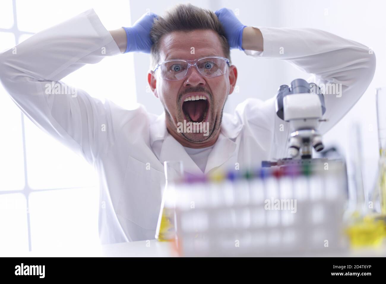 Mann in Schutzbrille und Gummihandschuhe zieht die Haare an Sein Kopf im chemischen Laborportrait Stockfoto