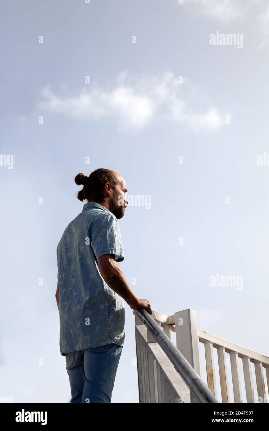 Bärtiger Mann in kurzen Ärmeln und Jeans stehen am Geländer Stockfoto
