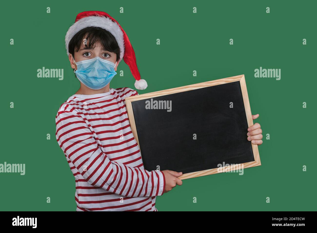 Frohe Weihnachten, lustiges Kind mit medizinischer Maske, die eine Tafel hält Grüner Hintergrund Stockfoto