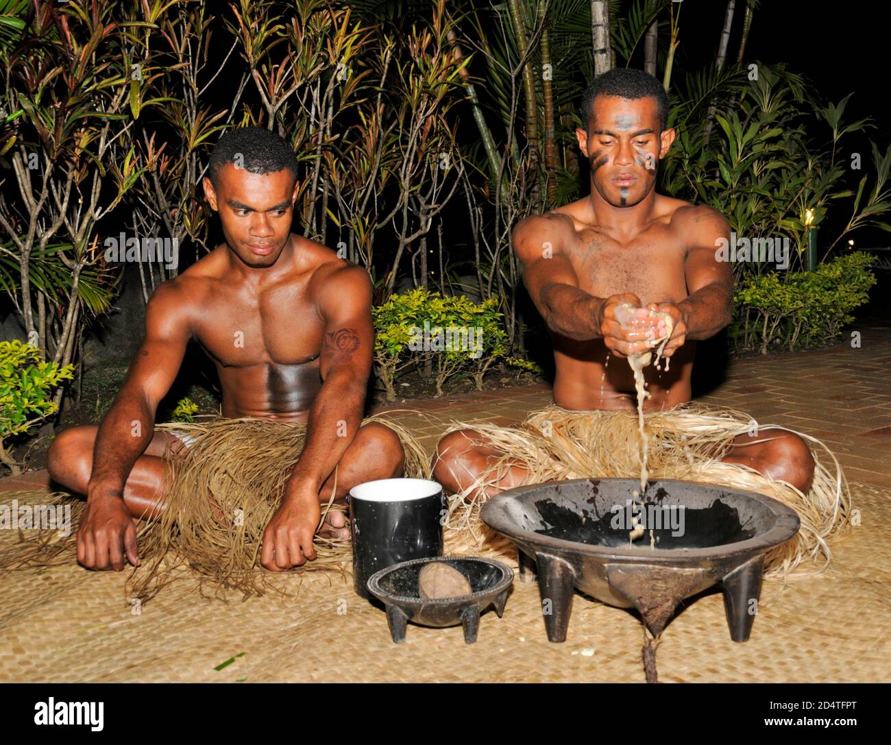 Zwei Fidschianer hocken auf Matten bei einer Touristenshow, um Fijis Nationalgetränk, Yaqona, auch Kava in Fidschi im Südpazifik genannt, zu servieren. Yaqona oder Kava Stockfoto