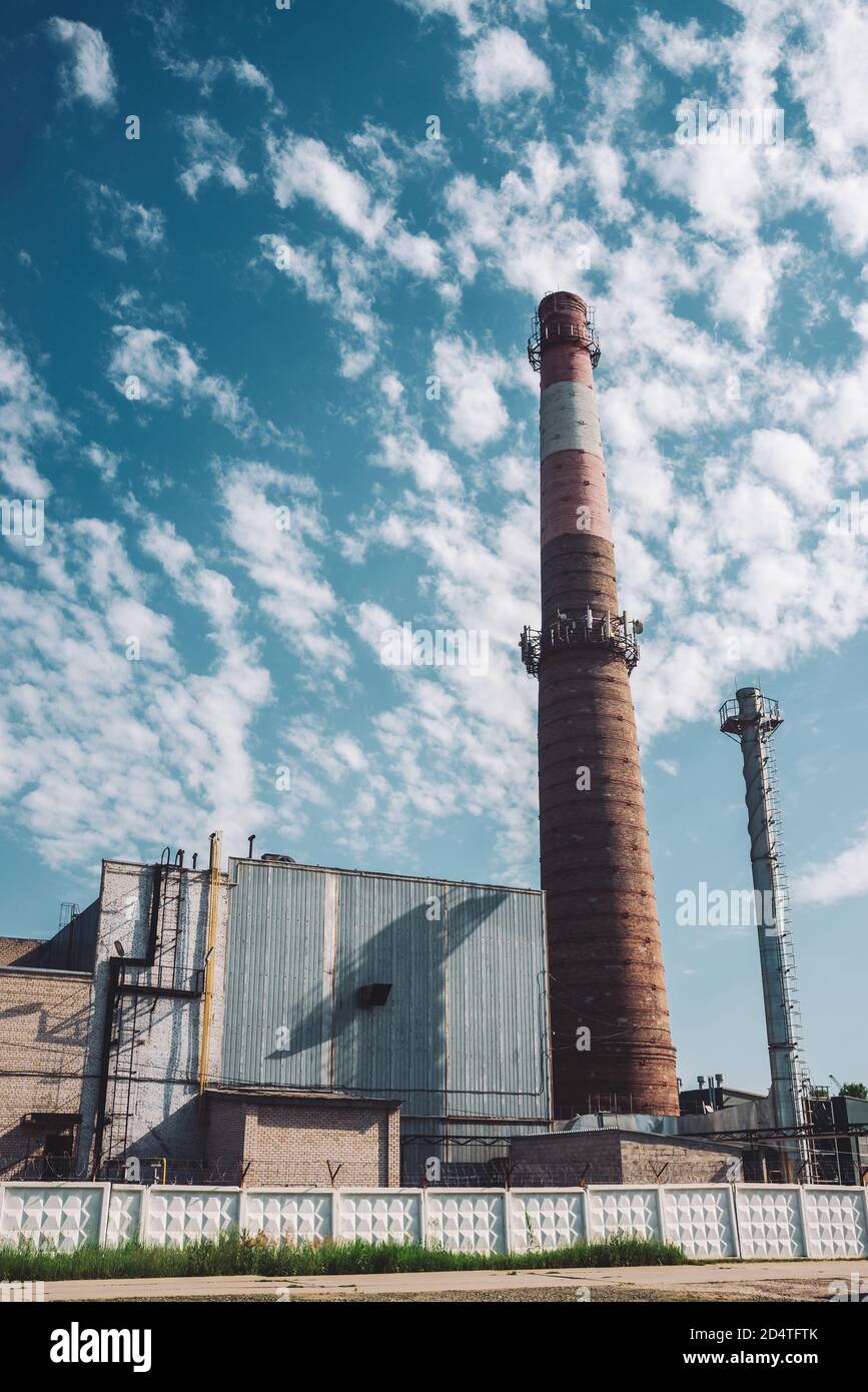 Riesiger Rauchstapel macht Wolken am Himmel an sonnigen Tagen. Industriegebäude mit großem Rohr aus braunem Ziegelstein unter blauem Himmel. Fertigungsgebäude in der Industriestraße Stockfoto