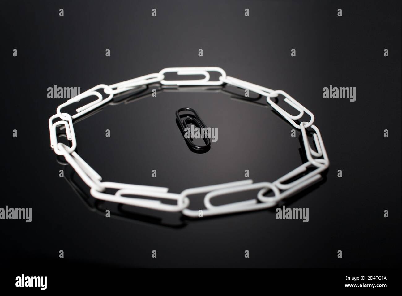 Ein Kreis von Büroklammern mit einer in der Mitte, die nicht passt in und wird von den anderen umgeben. Symbolische Darstellung von nicht passend in der gr Stockfoto